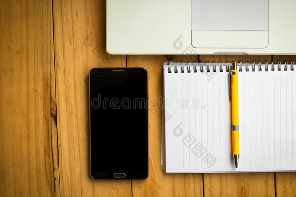 空白笔记本和一支黄色钢笔，上面有手机和笔记本电脑