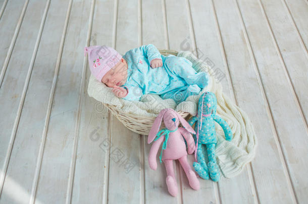 可爱可爱的可爱宝贝女孩睡在白色篮子在木地板上，有两只玩具蒂尔达兔子
