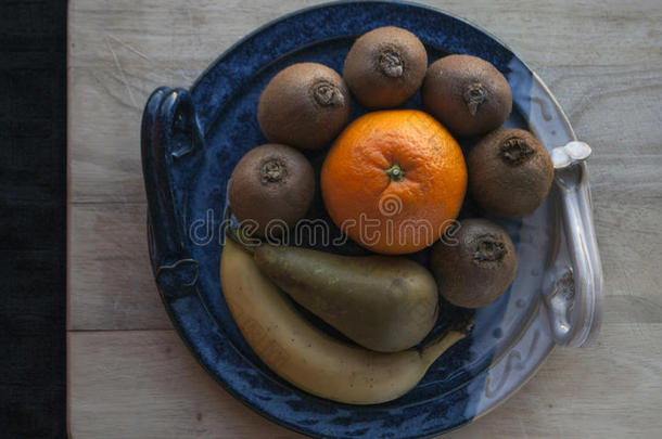 水果的组成在装饰蓝色盘子上的木板上，背景是黑色的布