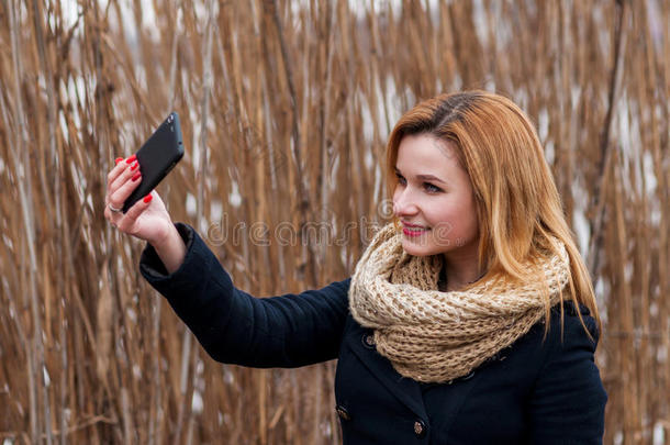 特写美丽的年轻女人在户外用智能手机自拍照片