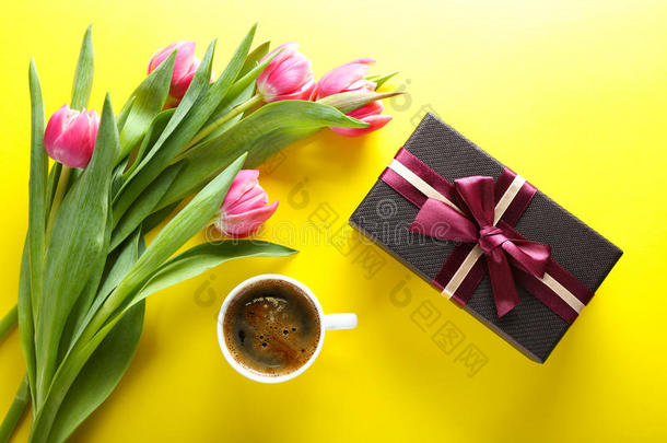 一杯咖啡，礼品盒和黄色背景上的粉红色郁金香