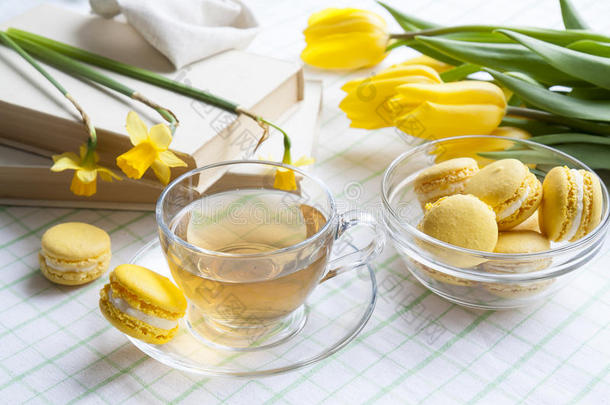 一杯热茶，黄色郁金香，黄色水仙花，旧书和柠檬马卡龙在一个轻的背景