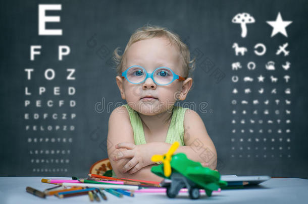 戴眼镜的孩子坐在<strong>桌子</strong>后面的<strong>桌子</strong>旁做眼科检查