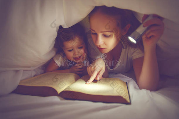 家庭阅读睡前。 妈妈和孩子在毯子下面用手电筒看书
