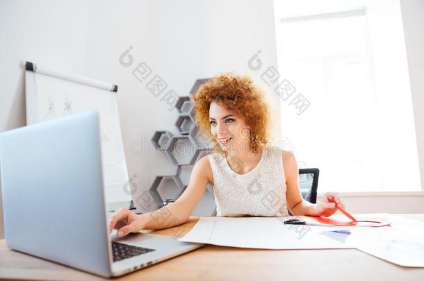 开朗的女人在办公室里<strong>剪彩</strong>色纸和使用笔记本电脑