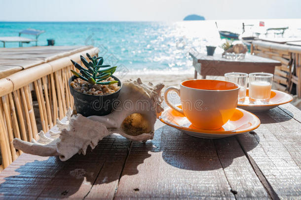 在美丽的早晨<strong>阳光下</strong>，海滩前的木桌上的咖啡杯