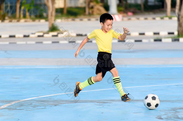 男孩在蓝色混凝土地板上踢足球。