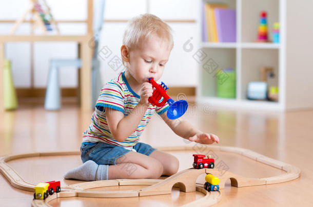 孩子们在托儿所的地板上玩木铁路。 小男孩玩一根管子想象火车司机给的东西