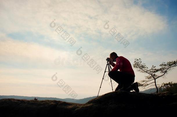 业余摄影师在岩石的山顶上用镜子照相。梦幻多雾的风景，春天橘红色薄雾的日出