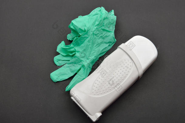黑色背景下的脱毛蜡加热器美容装置上的绿色手套和白色装置上。 脱毛。 准备