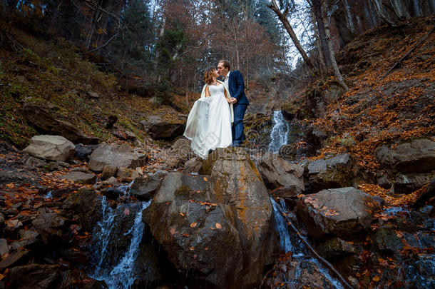 美丽的新婚夫妇在瀑布上接吻。 在秋山度蜜月