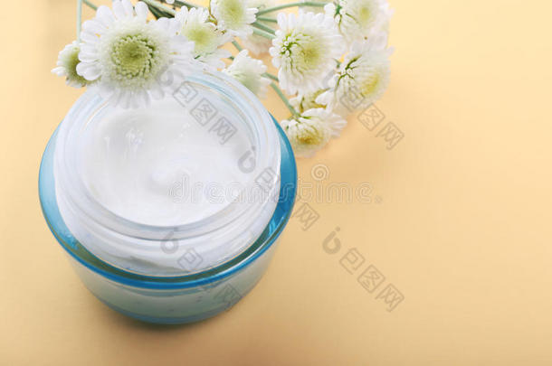 玻璃罐与面部或身体奶油和花在米色背景
