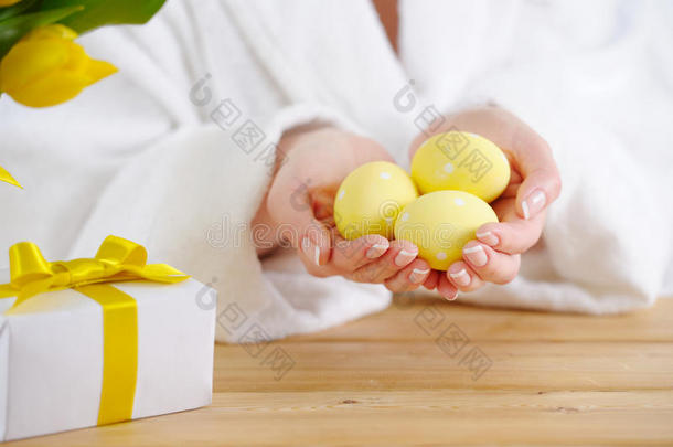 复活节。 女人穿着白色浴袍，手里拿着鸡蛋。 桌子上有黄色郁金香。