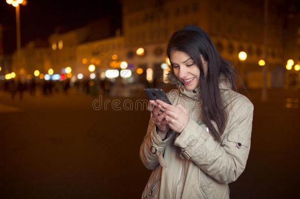 兴高采烈的女人使用她的智能手机和微笑的好消息。 快乐的女人在智能手机上键入短信