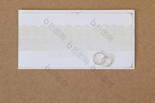 两枚戒指在一张结婚邀请函上，上面有白纸花边丝带