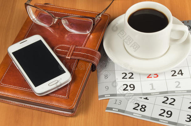 木制桌子上的咖啡、手机、眼镜、规划师和日历