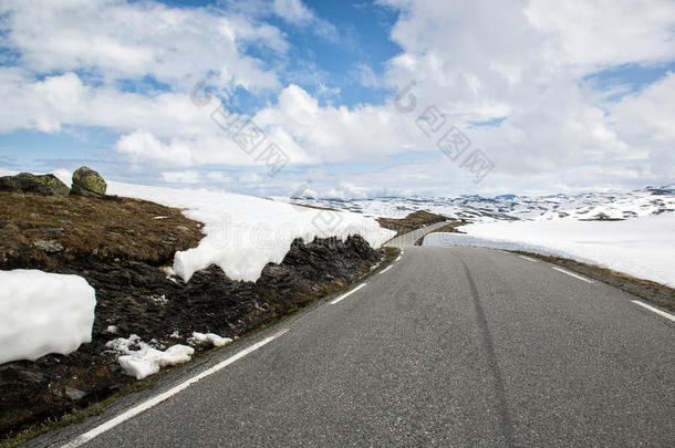 沥青路穿过群山，有很多雪，夏天的挪威。 国家旅游路线极光