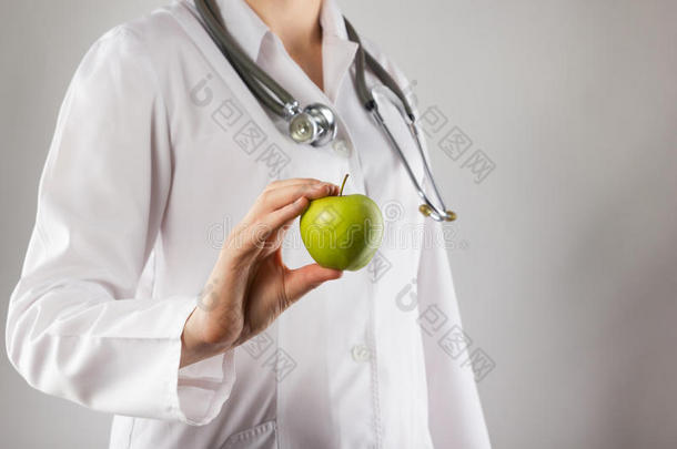 女医生手里拿着绿苹果。 特写镜头在灰色