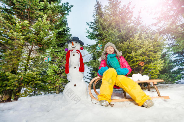 女孩坐在雪橇上，在森林里堆雪人