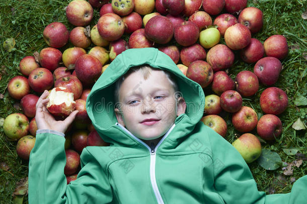 一个<strong>金</strong>发男孩躺在绿色的草地上，拿着<strong>苹果</strong>，吃着，咬着<strong>苹果</strong>