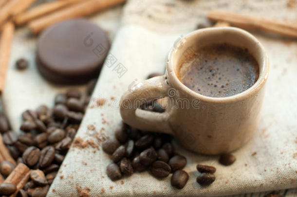 一种由手工制作的陶器杯咖啡、肉桂棒、咖啡豆、可可粉和巧克力糖果组成的组合物