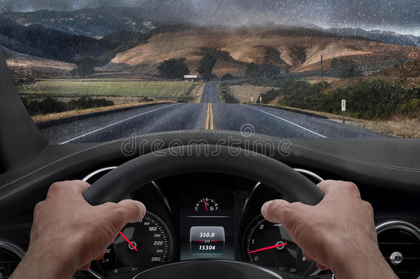 在雨天开车。 从司机的角度看，而手在车轮上。 雨溅了挡风玻璃
