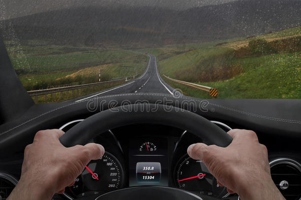 在雨天开车。 从司机的角度看，而手在车轮上。 雨溅了挡风玻璃