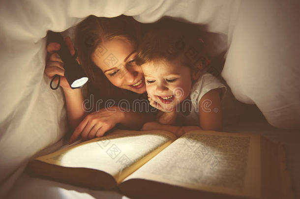 家庭阅读睡前。 妈妈和孩子在毯子下面用手电筒看书