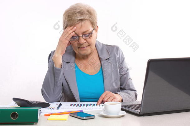 老年商业妇女牵着她的头，在办公室的办公桌上工作，商业理念