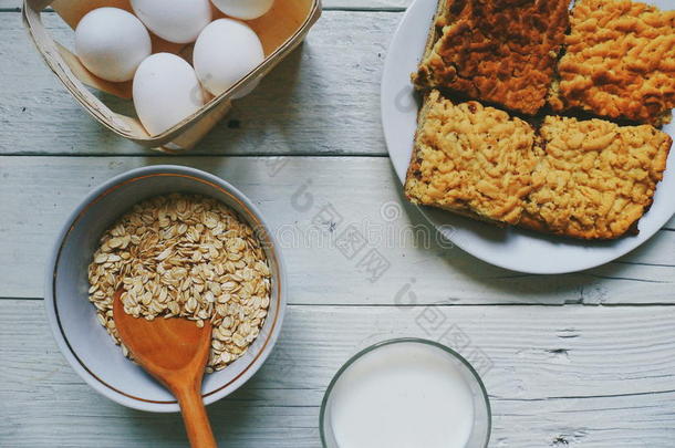 一杯牛奶，自制蛋糕，鸡蛋和燕麦片放在白色桌子上的碗里