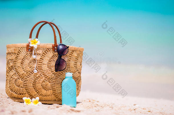 海滩配件-稻草袋，耳机，瓶奶油和太阳镜在海滩上
