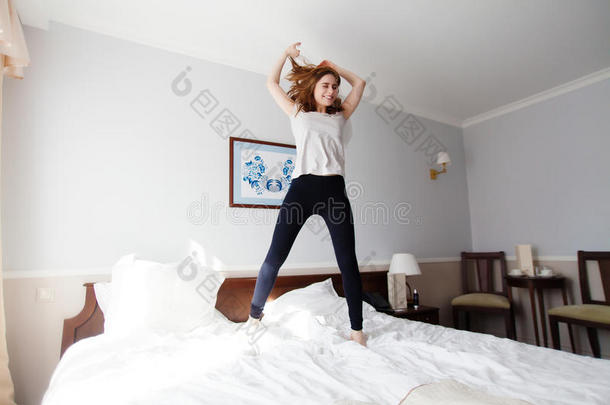 漂亮的年轻女孩在酒店的双人床上跳得很有趣
