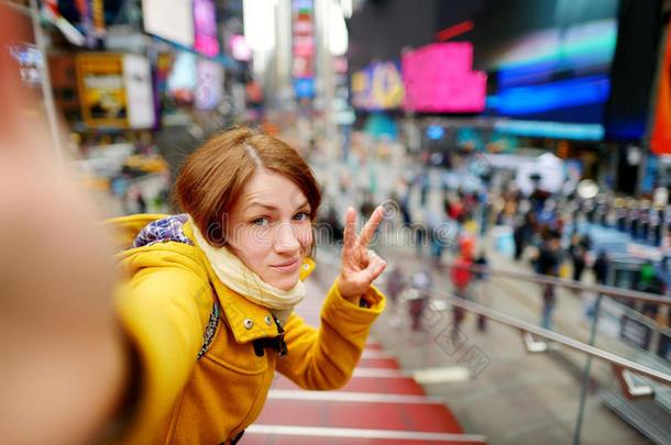 美丽的年轻女人在时代广场用她的智能手机自拍
