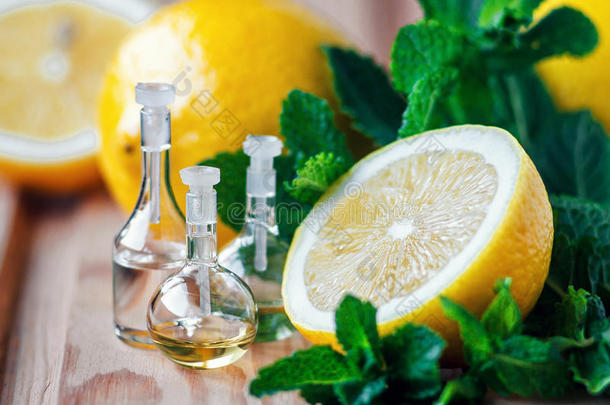 玻璃瓶中的精油，有新鲜多汁的柠檬水果和木制背景上的薄荷绿叶。 美容治疗。