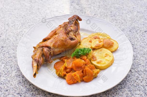 美味的烤兔腿与釉面甜胡萝卜和烤土豆在薄片上。