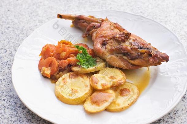 美味的烤兔腿与釉面甜胡萝卜和烤土豆在薄片上。
