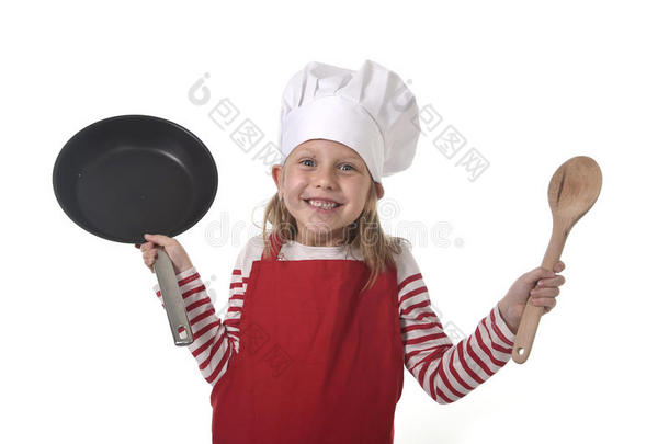 六七岁的小女孩戴着烹饪帽和红色围裙，玩着厨师微笑着拿着平底锅和勺子