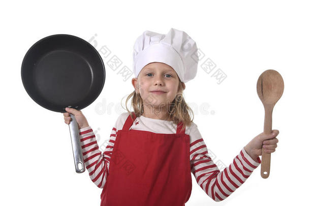 六七岁的小女孩戴着烹饪帽和红色围裙，玩着厨师微笑着拿着平底锅和勺子