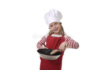 六七岁的小女孩戴着烹饪帽和红色围裙，玩着厨师微笑着拿着平底锅和勺子图片