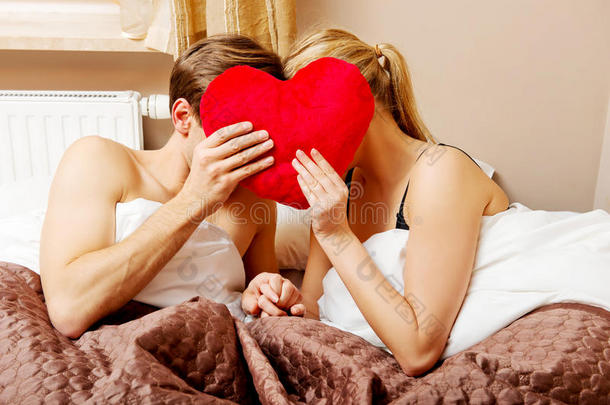 一对夫妇坐在床上，用心枕遮住脸