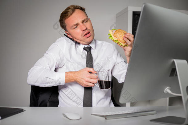办公室里一个忙着喝咖啡和吃汉堡的人