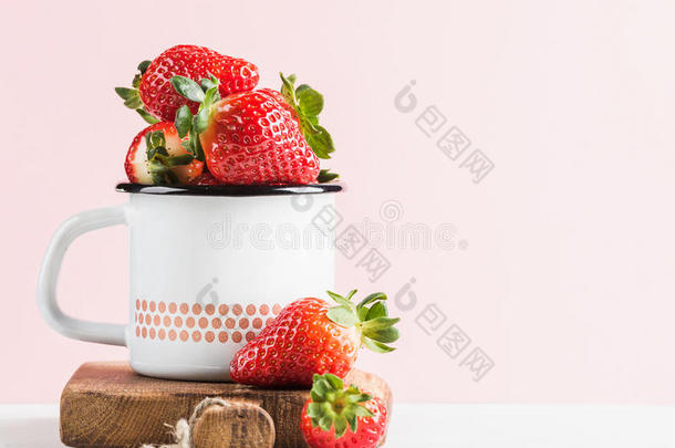 新鲜成熟的红色草莓，乡村风格的搪瓷杯在乡村木板上，<strong>淡粉</strong>色背景