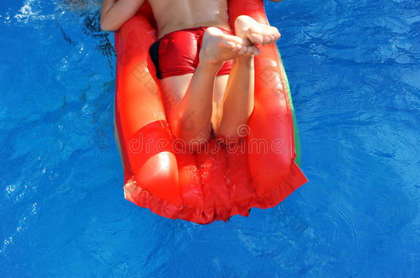 男孩穿着红色充气床垫在游泳池里