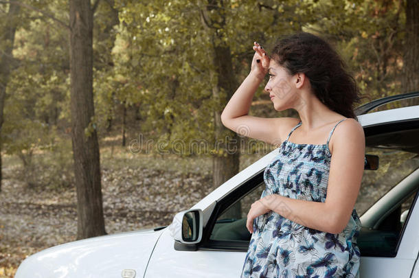 女孩站在乡间公路上，靠近汽车看着远方，大树高高的，夏天的季节