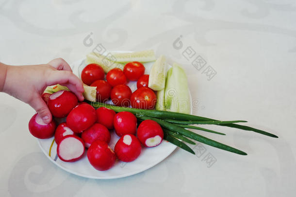 孩子的手在盘子与春天的蔬菜在白色装饰背景