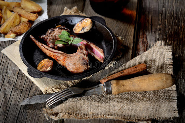 烤<strong>羊排</strong>与大蒜和草药在平底锅，老式刀和叉子在餐巾上的木制背景