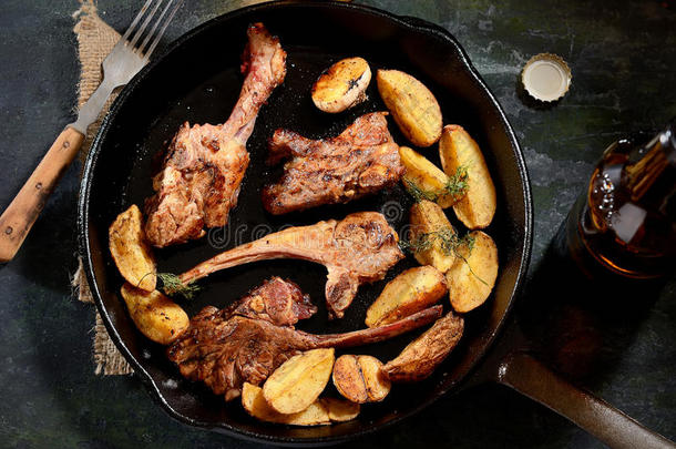 烤羊排与香料和油炸土豆在平底锅，老式刀和叉子在餐巾上的黑暗背景