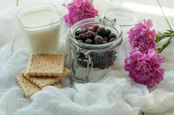一罐新鲜浆果，一杯自制酸奶，饼干和明亮的紫色花朵在精致的白色织物表面
