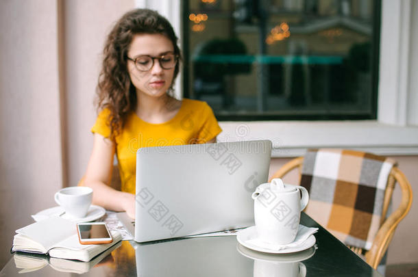 女孩戴着眼镜，带着笔记本电脑，在<strong>户外</strong>咖啡馆<strong>喝茶</strong>