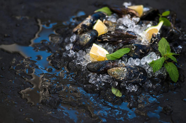新鲜未煮熟的贻贝与柠檬，草药和香料在碎冰上的<strong>黑色石板</strong>石背景